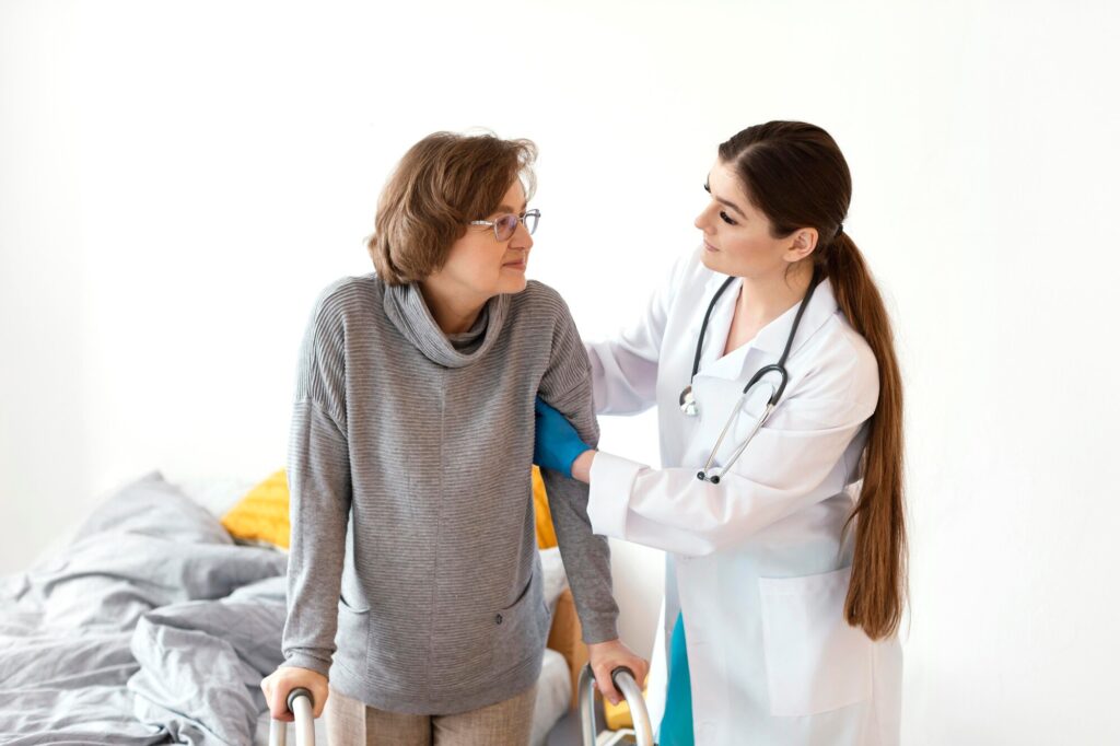 Female doctor assisting an older woman with mobility support during a medical visit.