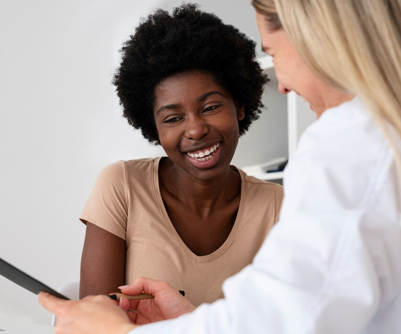 Smiling woman looking at a tablet with a healthcare professional during a consultation.